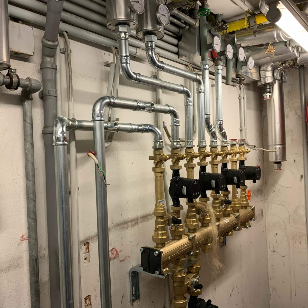 Detailansicht der komplexen Heizungsrohrleitungen und Verteiler im Technikraum des Fitnesscenters in 1110 Wien – professioneller Anlagenbau durch EMA Installationen. 